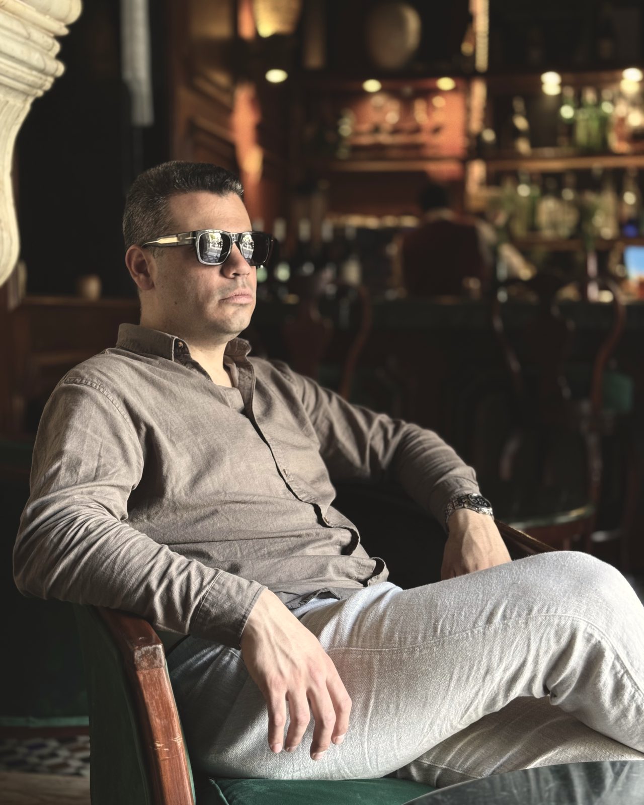 Orestis Vasileiadis seated in a wood-panelled bar in a linen shirt
