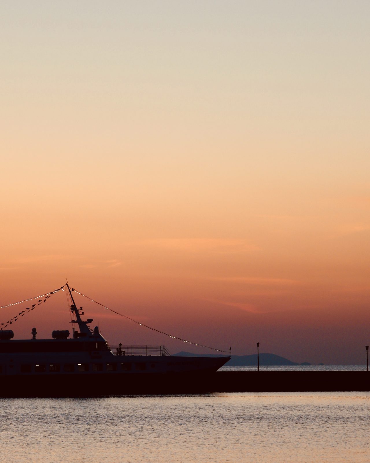 A ferry silhouetted against an orange Aegean sunset