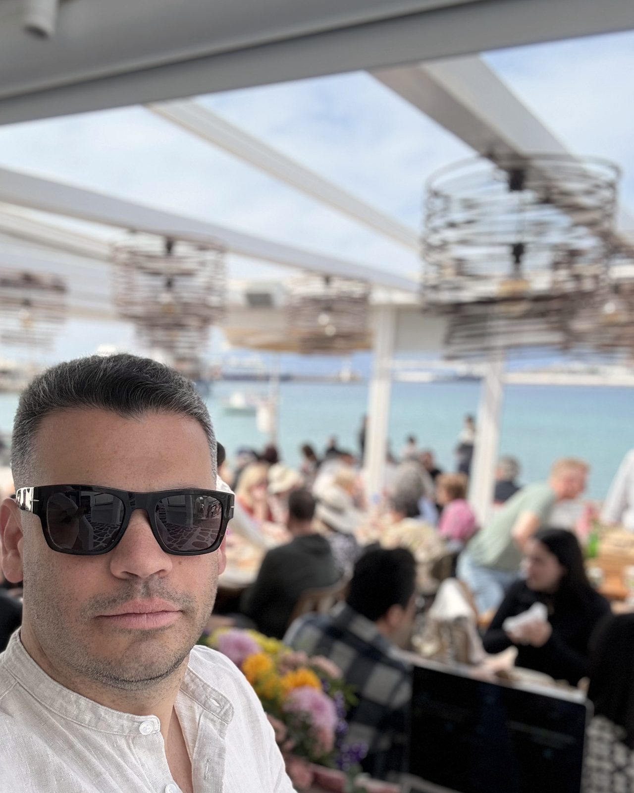 DJ Orestis at a seaside restaurant booth in daylight with diners seated behind